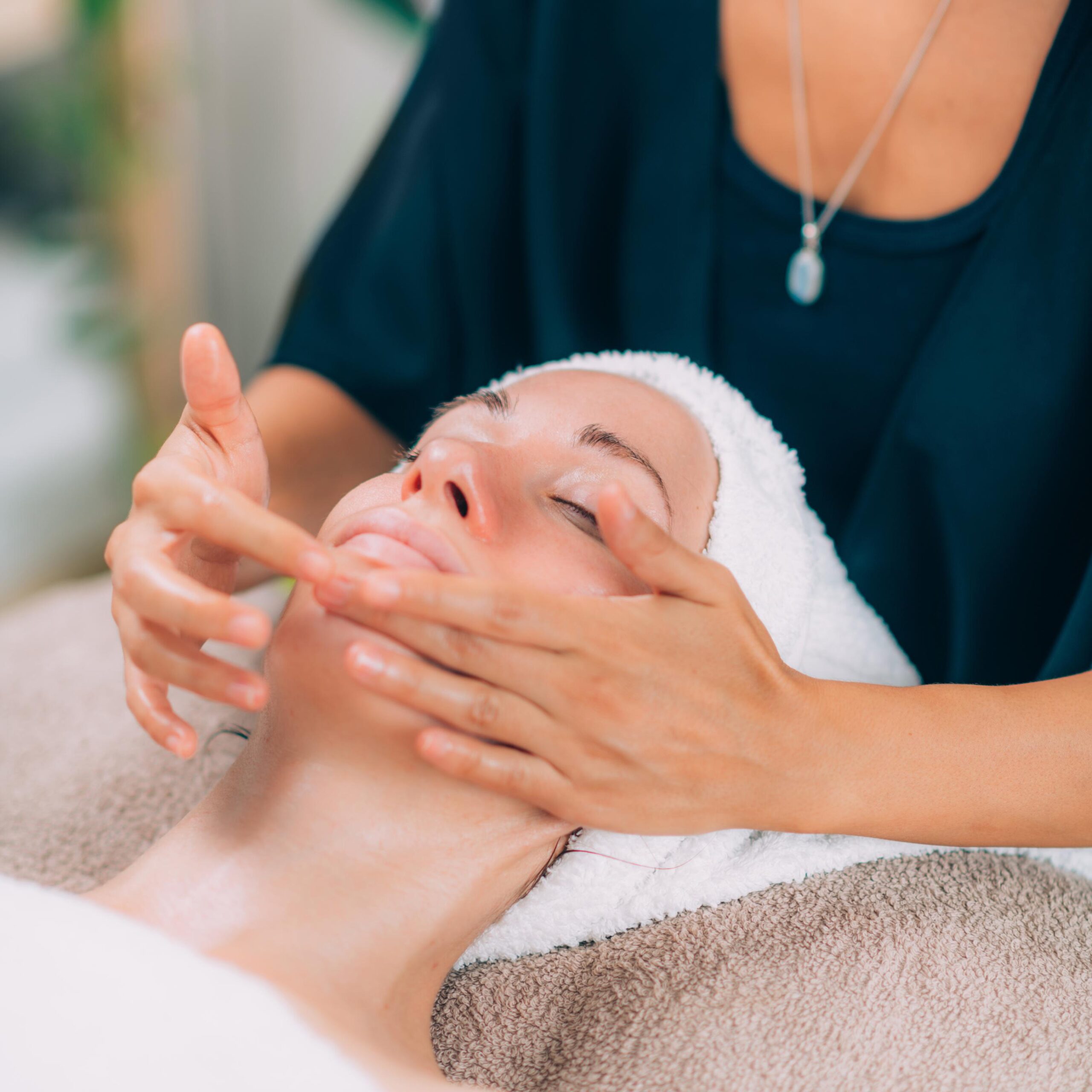 Woman with closed eyes enjoying a relaxing facial massage. A therapist applies cream to her face with gentle hands.